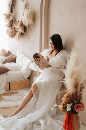 Serene scene with mother and baby in white dress surrounded by dried pampas grass and floral decorations.