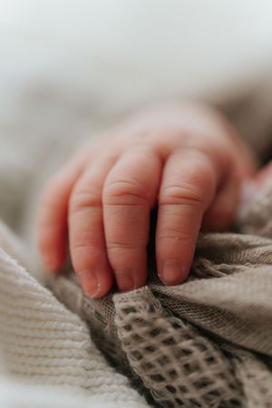 Close-up macro shot of a baby's tiny hand grasping textured knit fabric in soft focus.