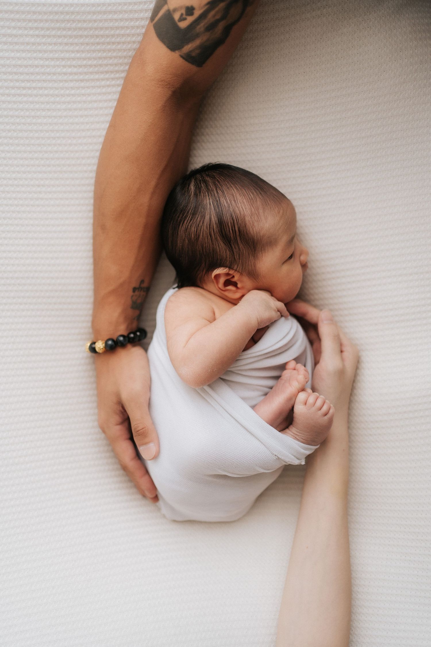 Gentle hands cradle a sleeping baby in white clothing against a soft textured background.
