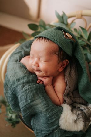 A sleeping newborn baby swaddled in emerald green linen fabric against a soft neutral background.