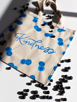 Canvas tote bag printed with blue blueberries and Kindness script surrounded by fresh blueberries.
