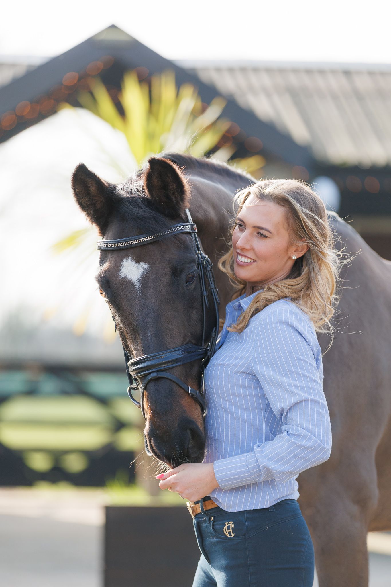 A brown horse and rider in a white sweater pose together against autumn foliage in soft natural lighting.
