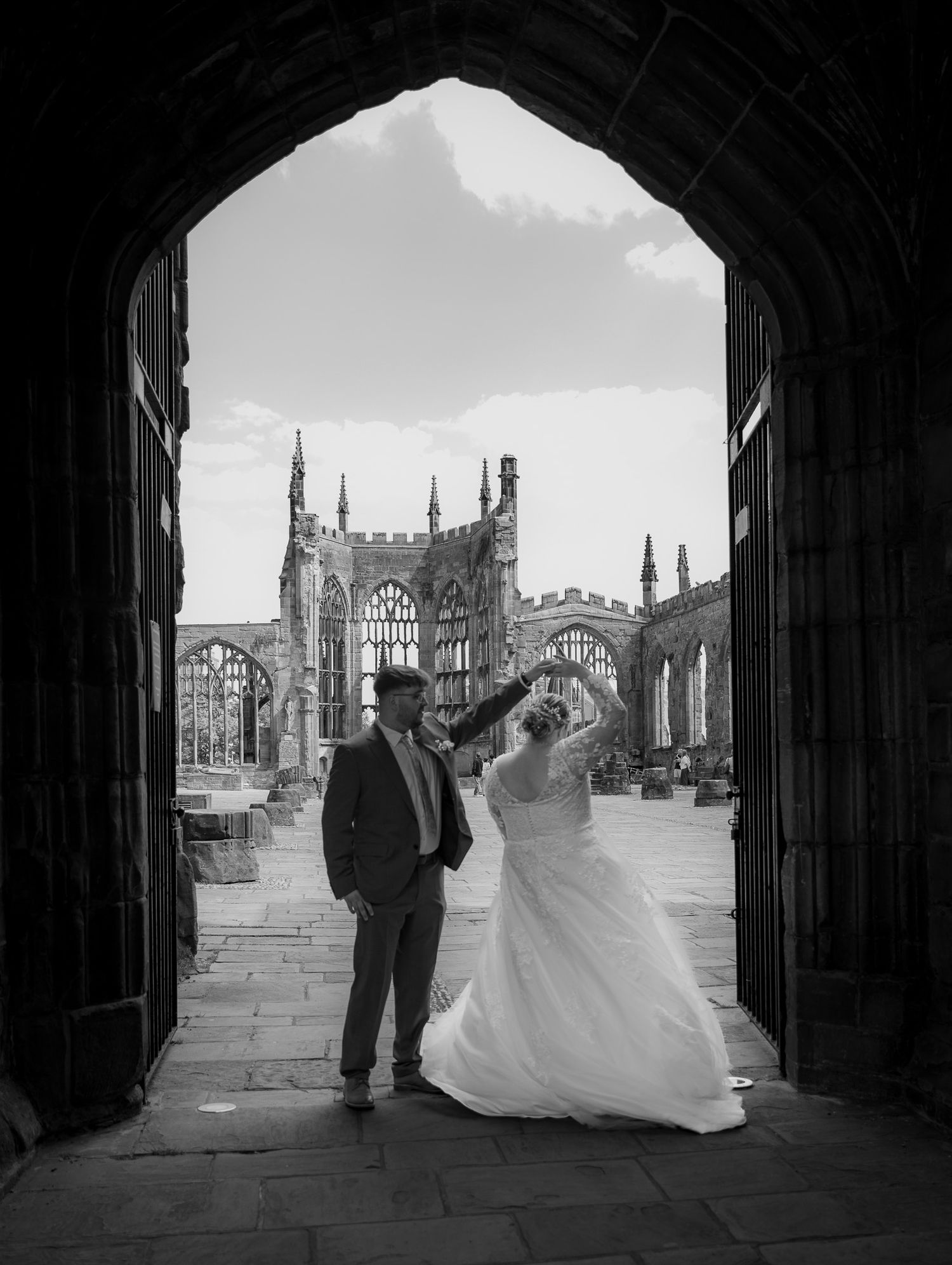 Newlyweds walk through confetti shower as guests with clear umbrellas celebrate in the rain outside a stone church.
