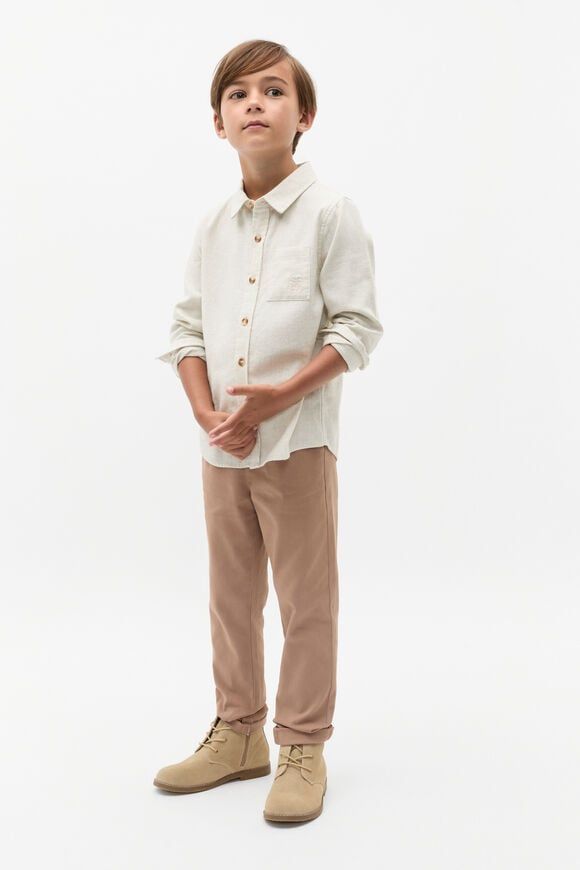 Boy wearing a white linen shirt with gold buttons, beige chinos, and tan suede boots on a white background.