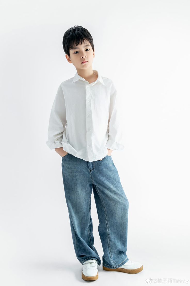 Young boy in a white long-sleeve shirt, wide-leg blue jeans, and white sneakers on a white background.