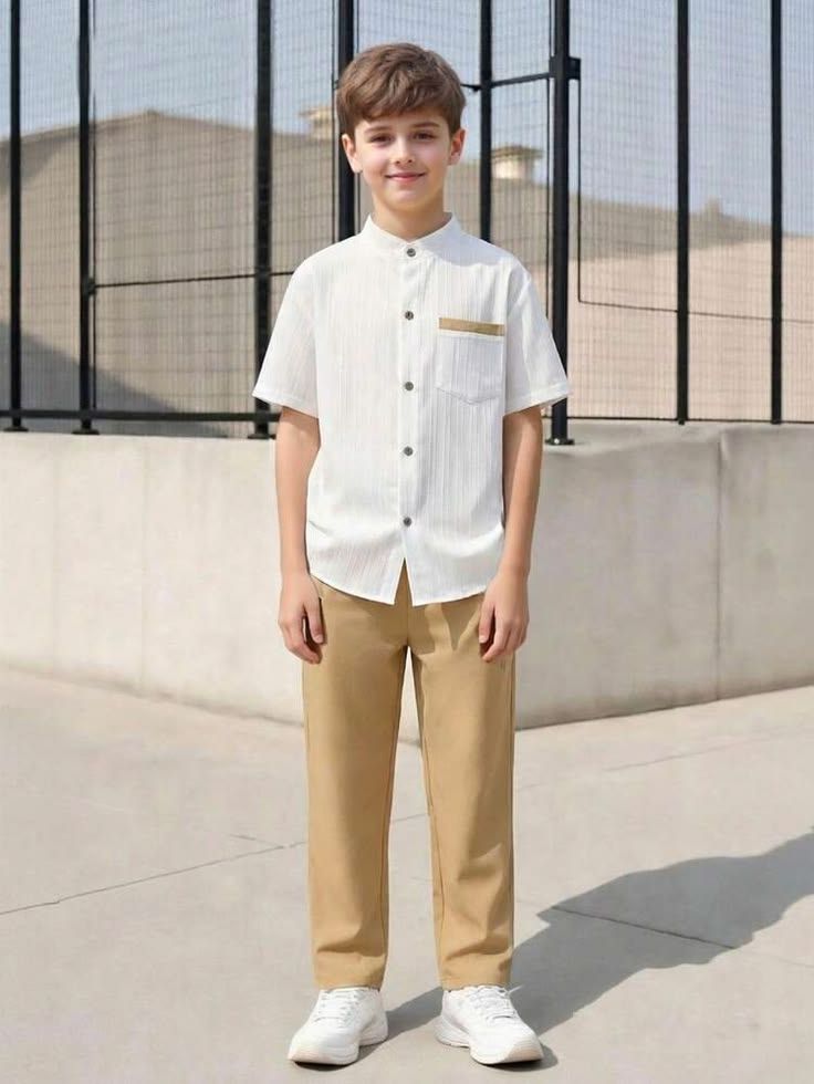 A young boy wearing a white short-sleeve button-up shirt with gold trim and khaki pants, paired with white sneakers.