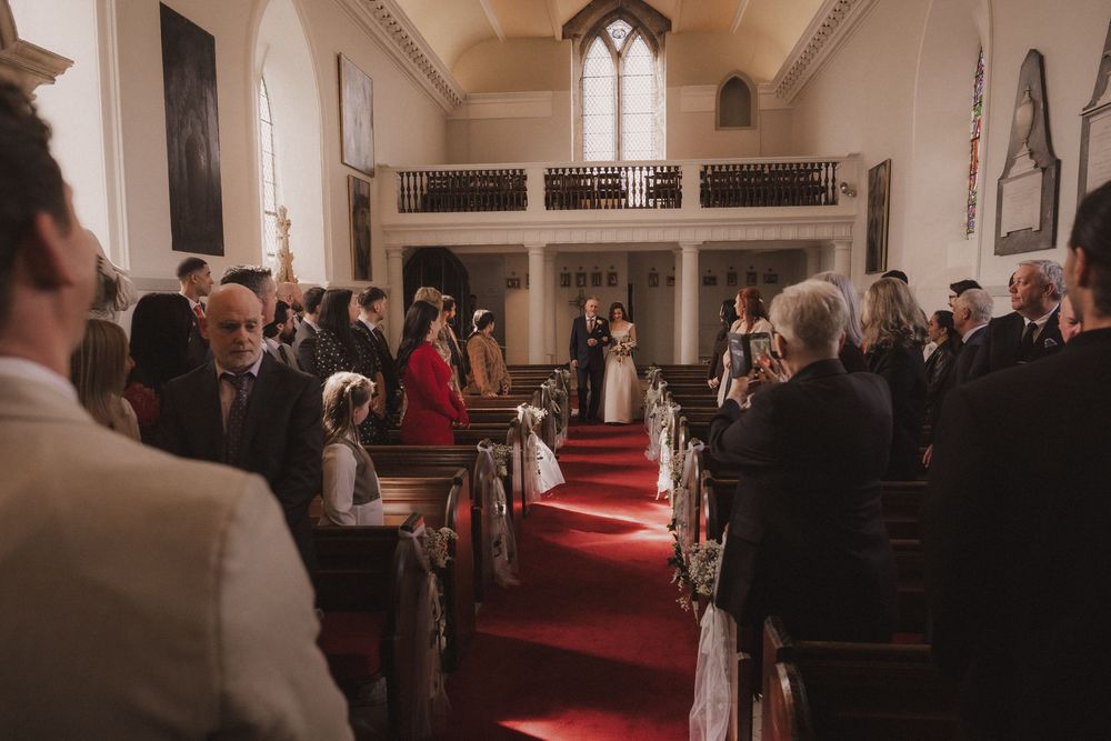 Wedding ceremony in a historic church with guests seated in wooden pews as the couple stands at the altar.