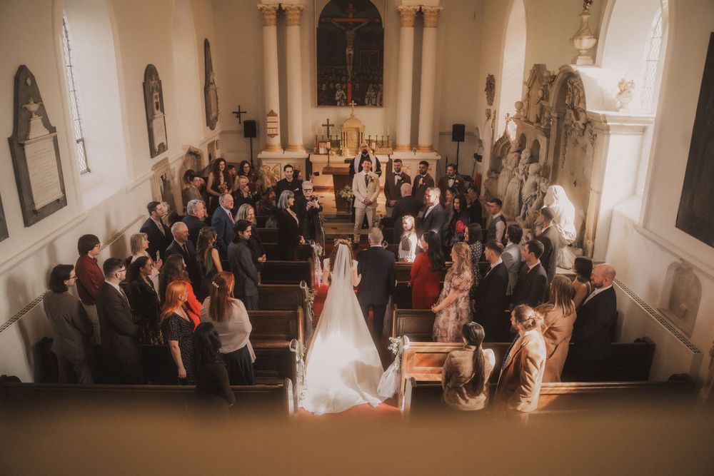 Aerial view of a wedding ceremony inside a historic church with guests seated in wooden pews.