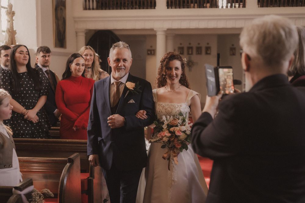 Bride walks down the aisle with her father in a sunlit church during wedding ceremony.