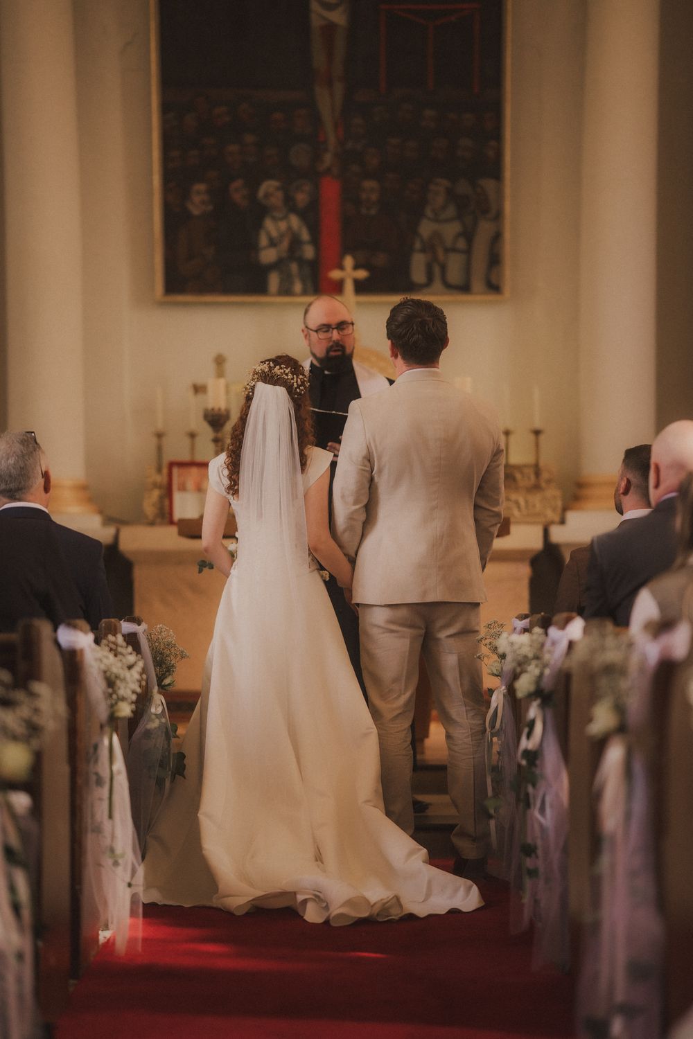 A bride and groom stand at the altar during a church wedding ceremony, with guests seated in pews on either side.