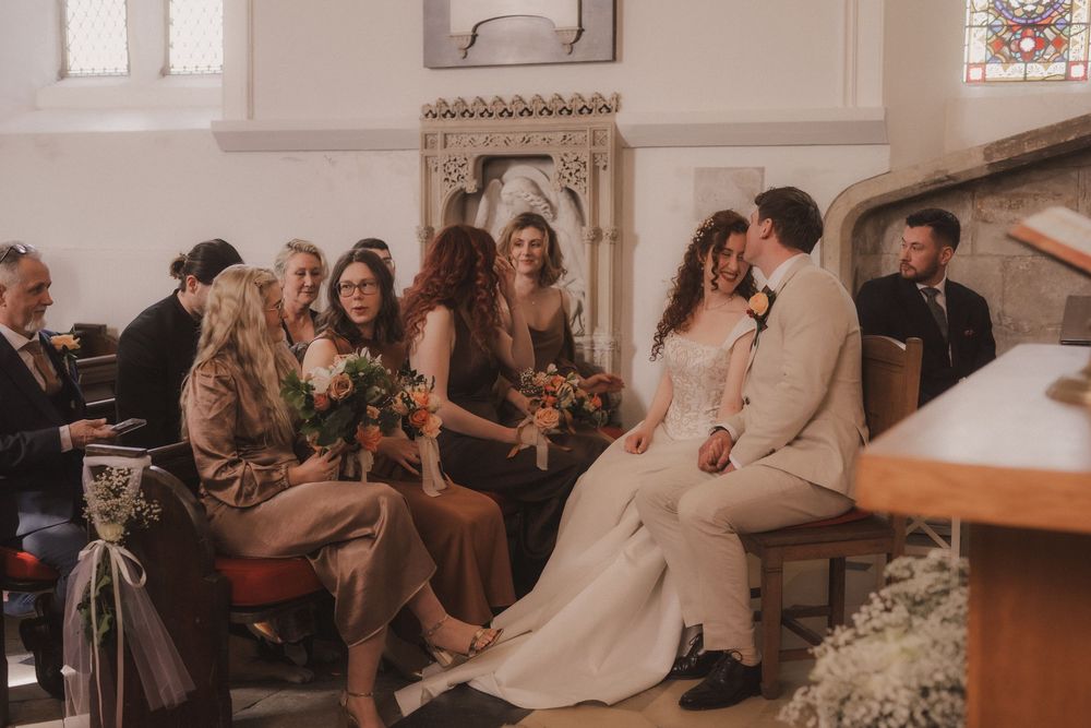 Bride and groom share a joyful moment with bridesmaids in a sunlit church during a romantic wedding ceremony.