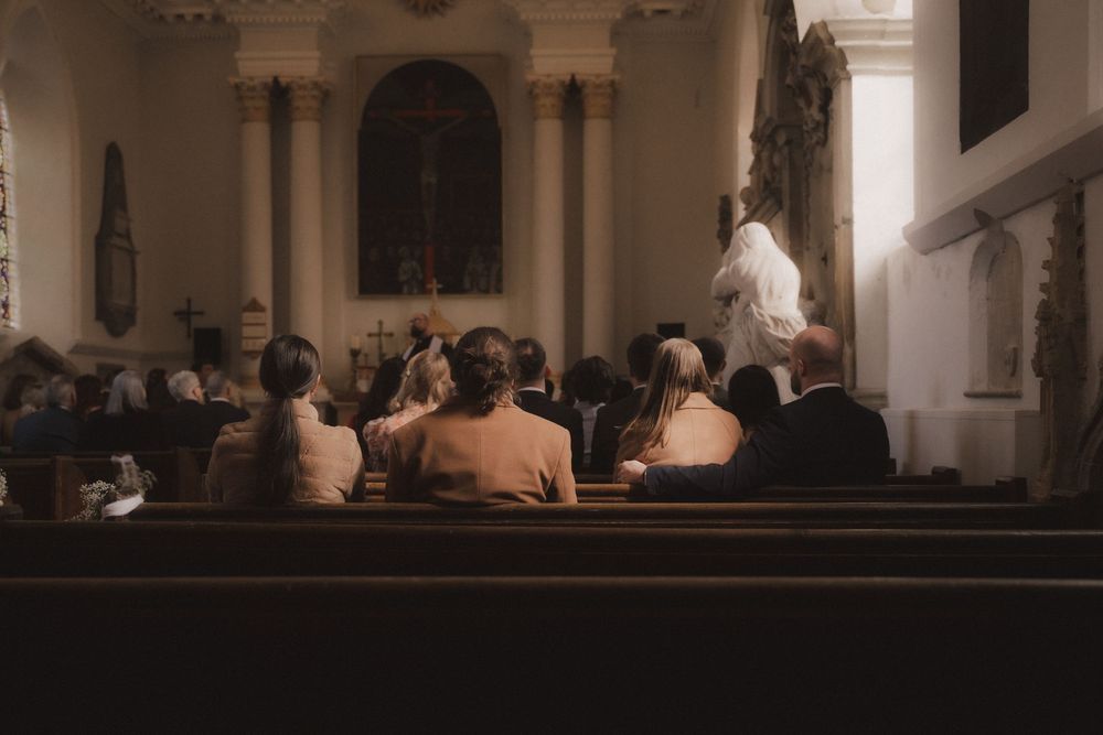 Congregation seated in wooden pews facing a priest at the altar inside a traditional Catholic church.