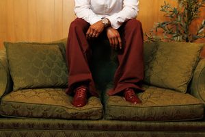 Person in burgundy pants and red sneakers sitting on a green velvet sofa near a potted plant.