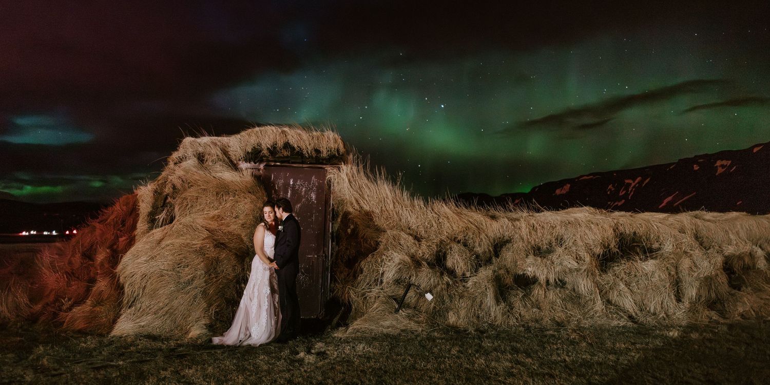 Bride and groom share a kiss under stunning green northern lights aurora borealis at night in Iceland.