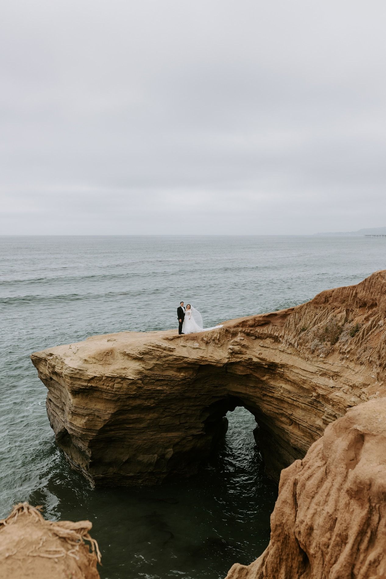 Bride and groom stand on dramatic coastal cliffs overlooking the ocean on their wedding day at Sunset Cliffs San Diego.