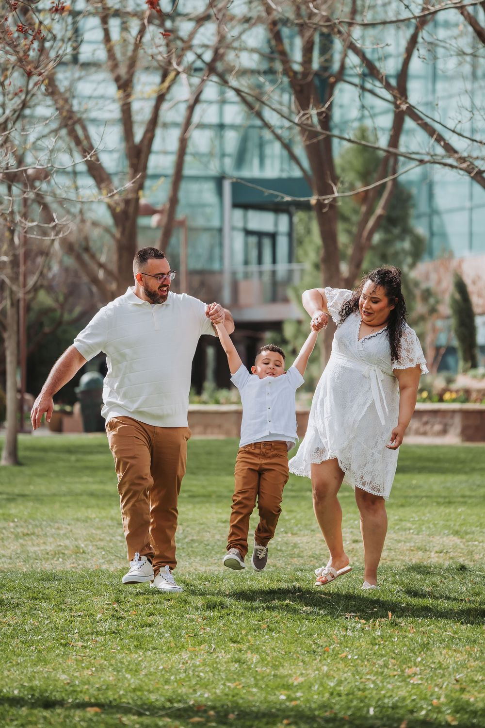 Family of three walking on grass, parents swinging young boy by hands outdoors.