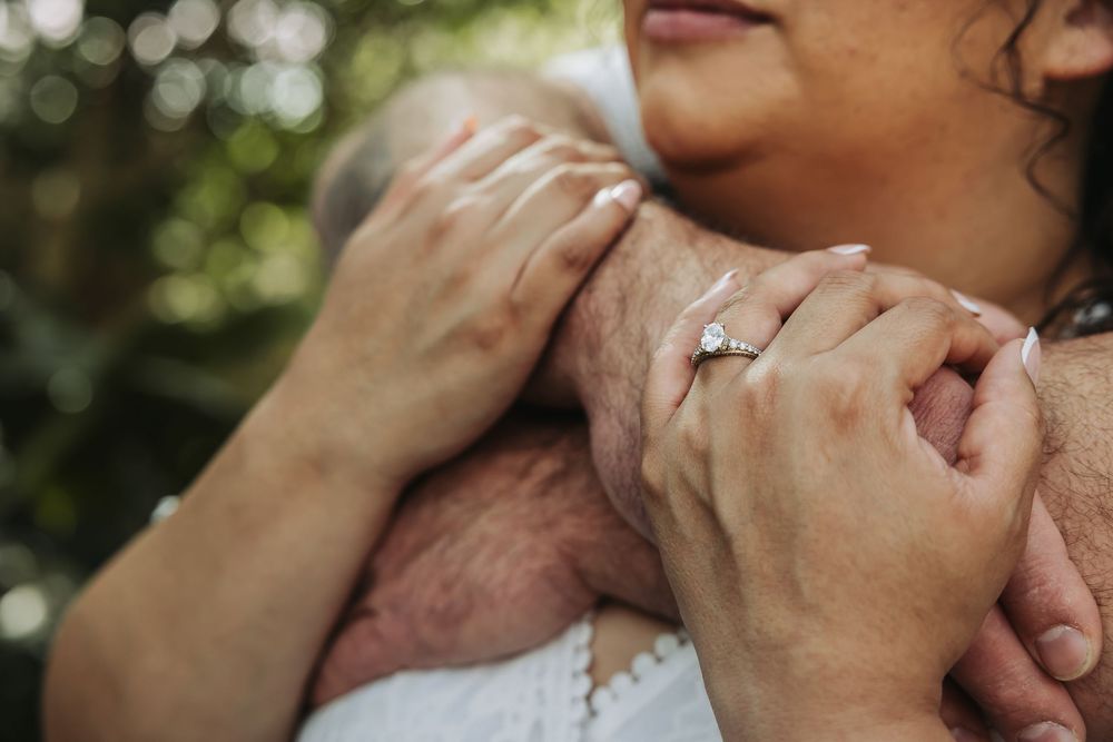 Close-up of a couple embracing, woman wearing a diamond engagement ring, romantic outdoor setting.