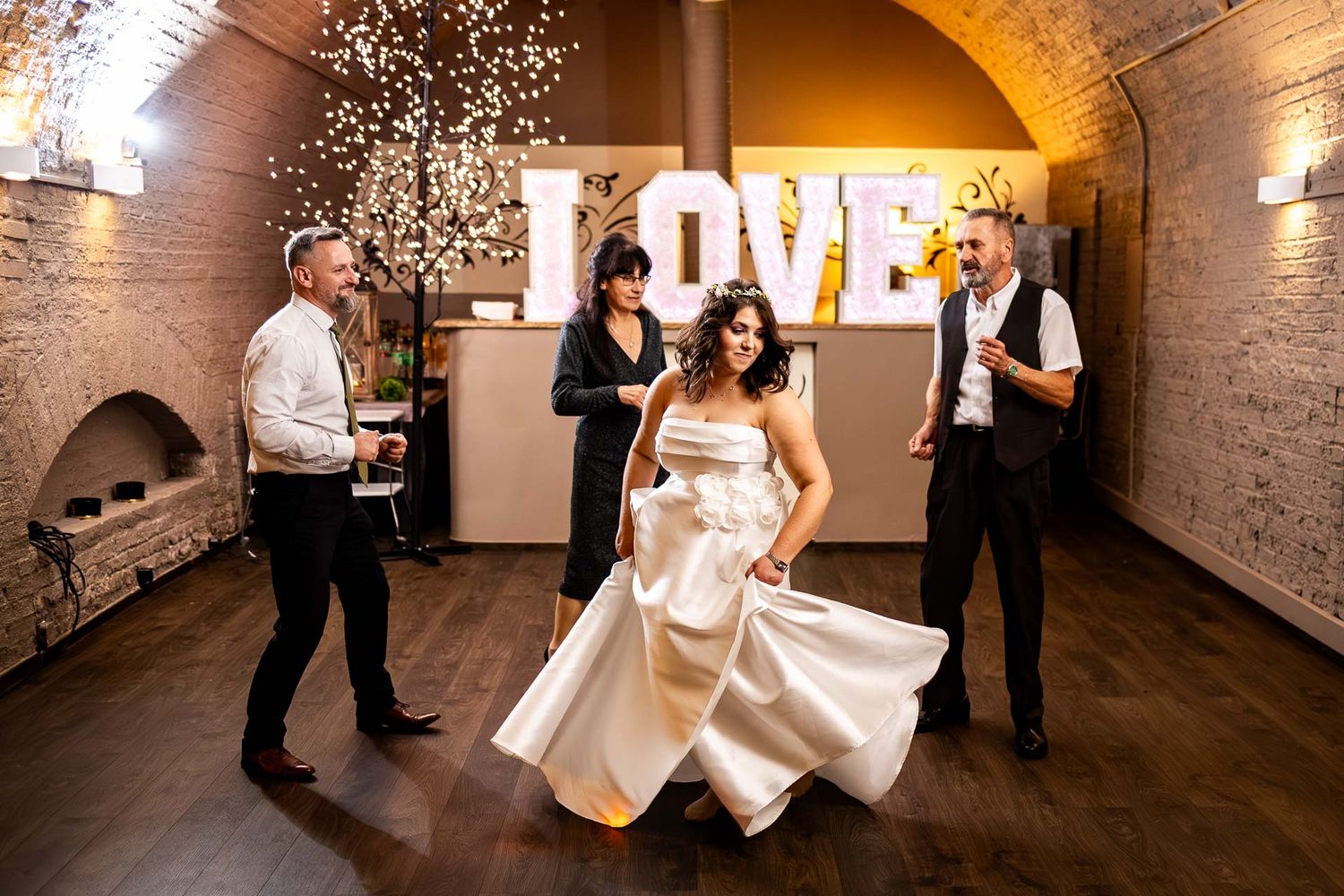 Wedding reception dance moves captured in a rustic venue with string lights and brick walls.