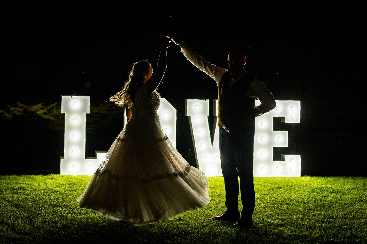 Dramatic nighttime wedding portraits with illuminated LOVE letters creating silhouettes.