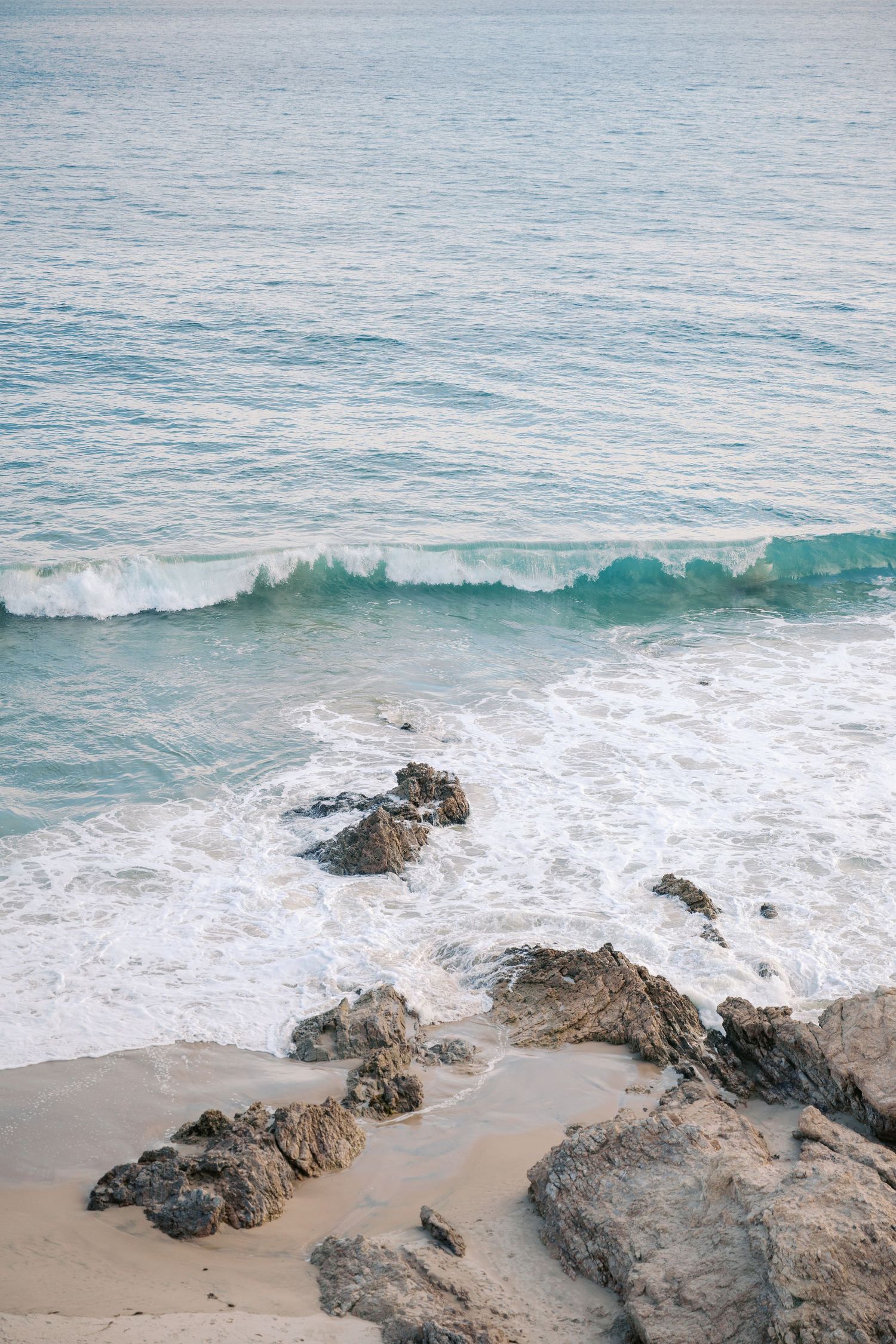 Turquoise ocean waves crashing over rocky shoreline on sandy beach.