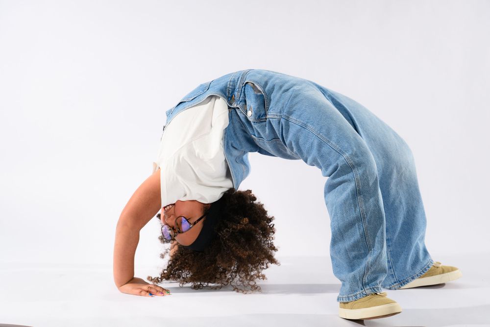Young person performing a backbend in wide-leg jeans and white top against a white background.