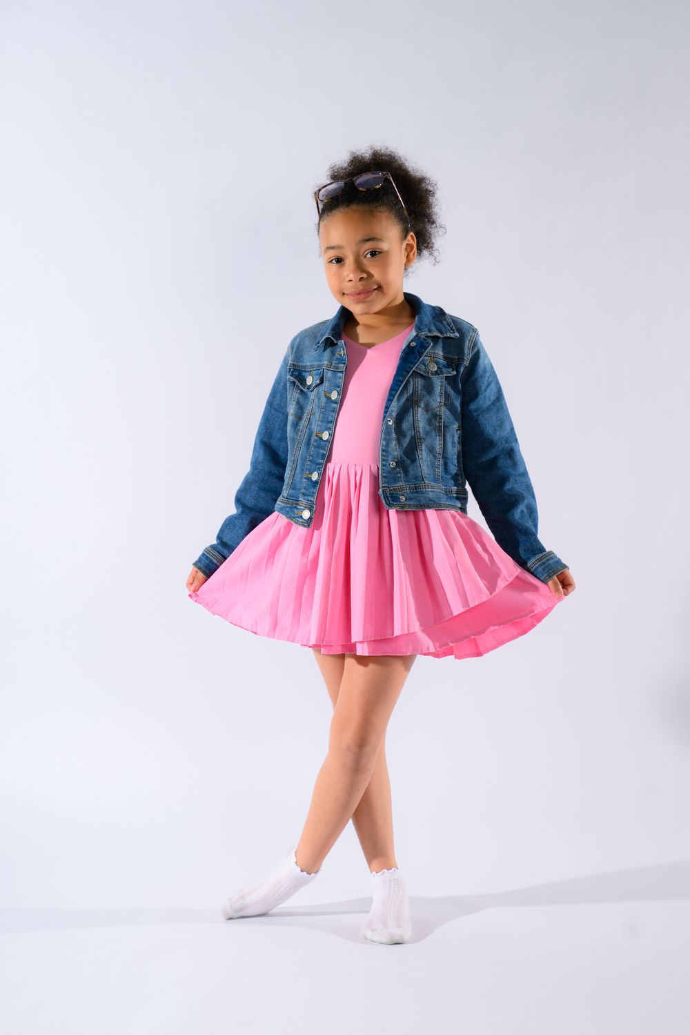 Cute African American girl in pink dress and denim jacket posing on white studio background.