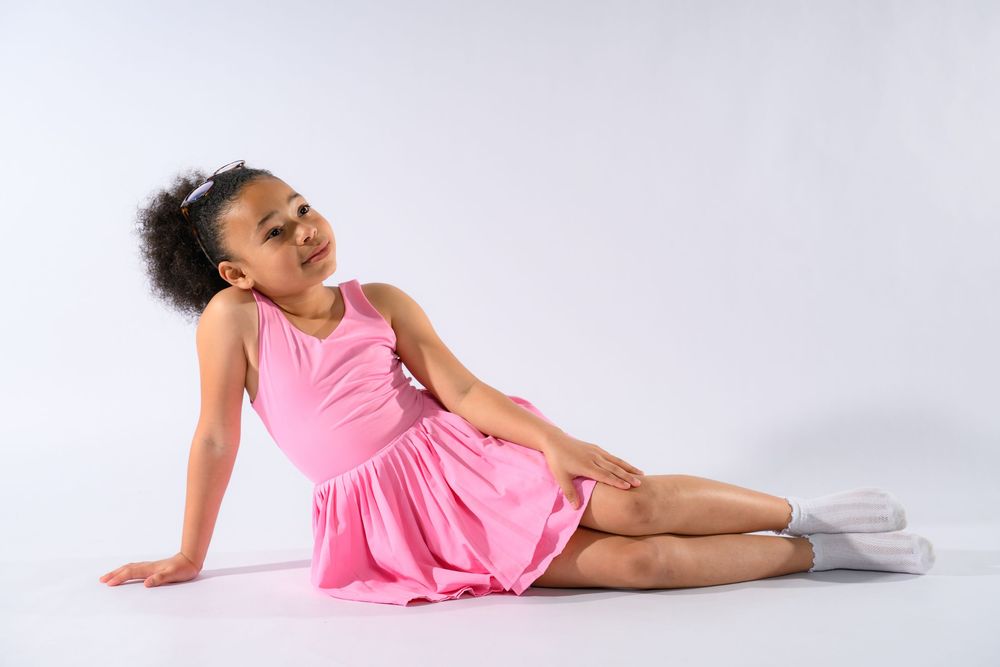 Young girl in pink sleeveless dress posing gracefully on white studio floor.