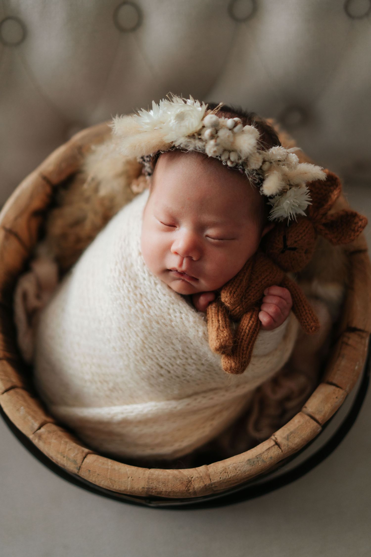 香港專業 newborn photographer 拍攝作品Sleeping newborn baby swaddled in white wrap wearing floral crown resting in wooden basket.