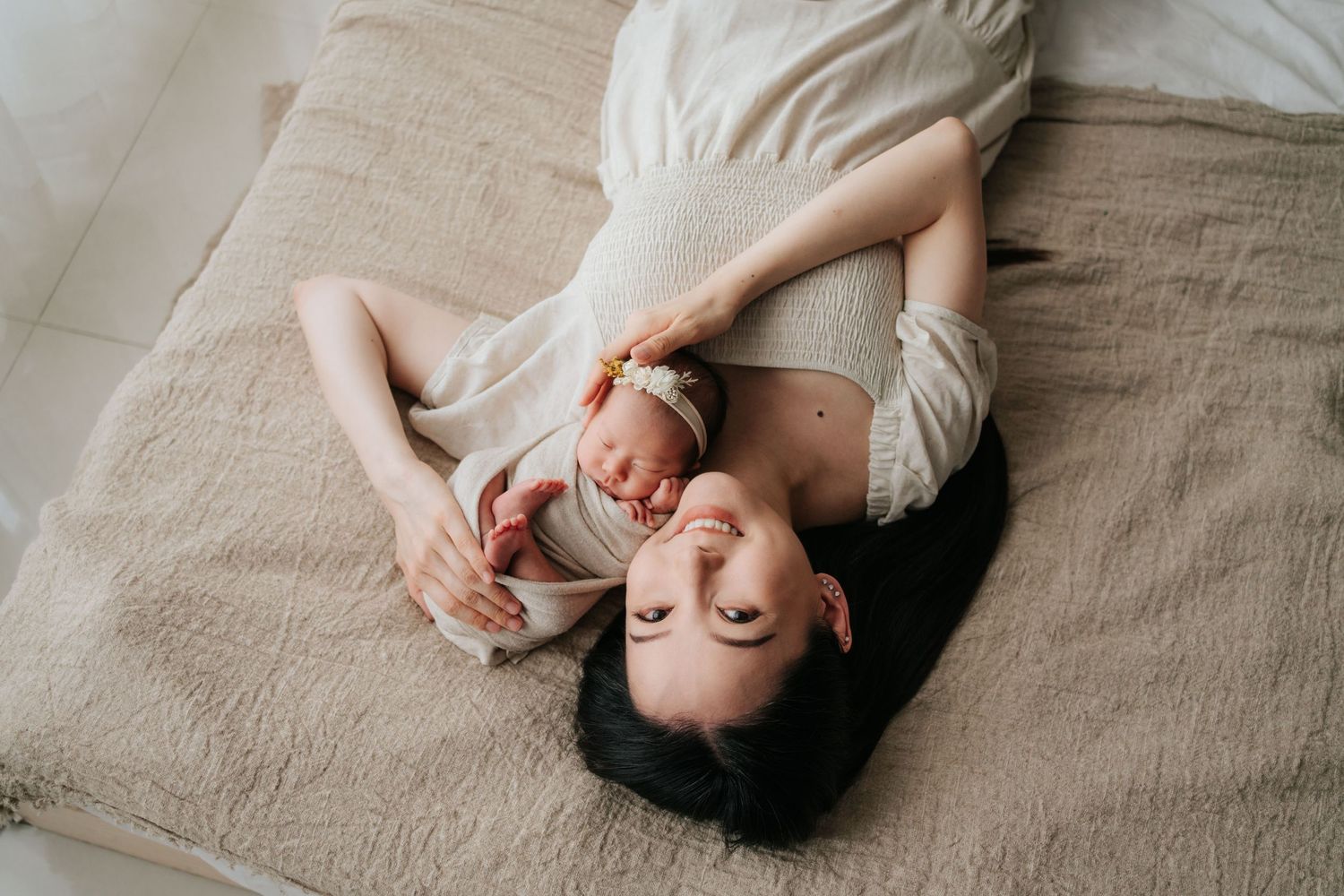 溫馨 newborn family photography，記錄初Mother lying on bed with her newborn baby, sharing a tender moment in a bright, minimalist bedroom setting.
