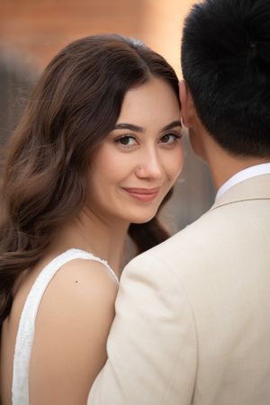 Close-up portrait of a smiling bride with brown hair leaning against her groom in a beige suit.
