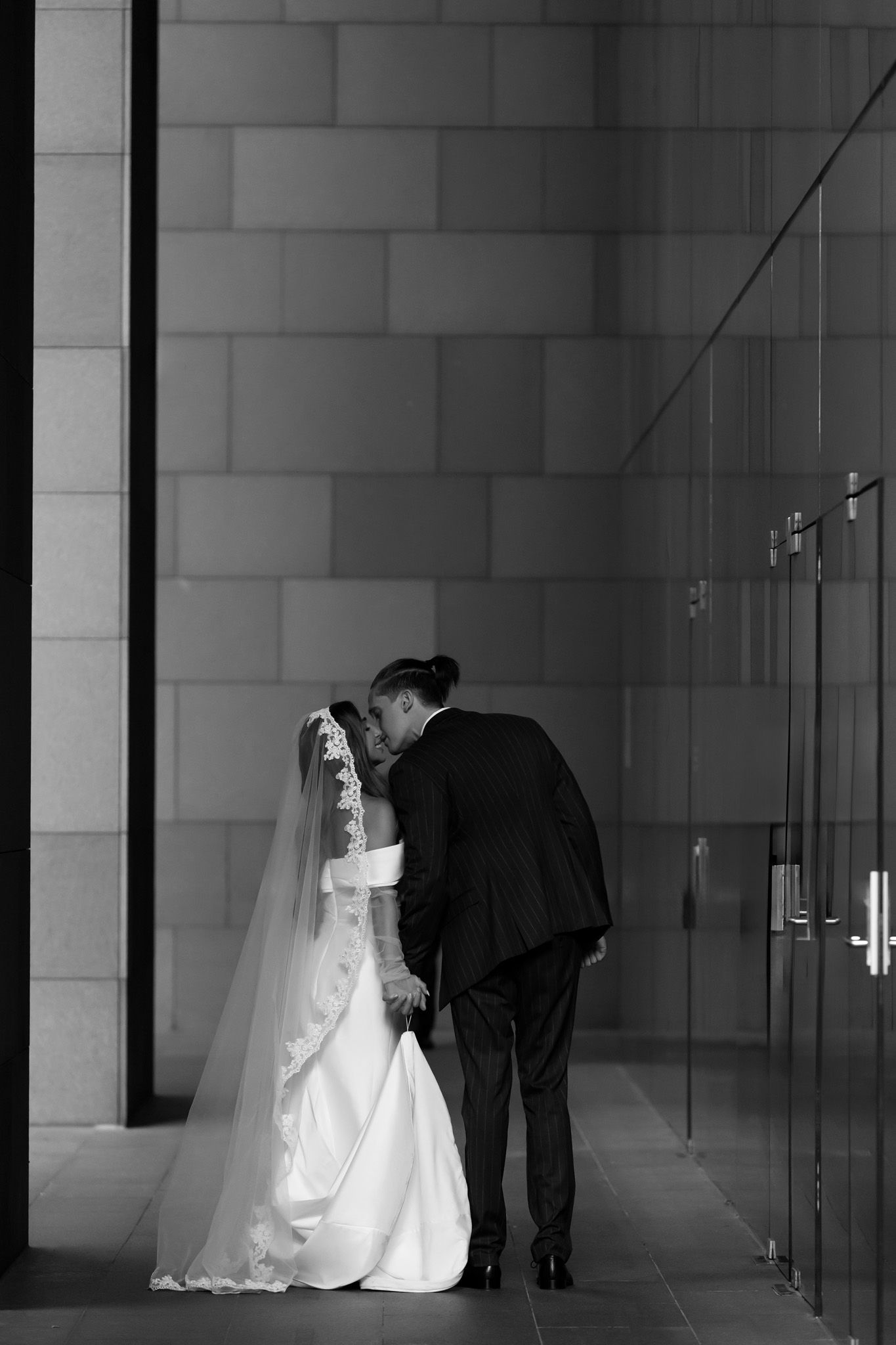 Black and white photo of bride and groom sharing an intimate moment in a modern architectural setting.