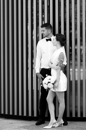 Black and white photo of bride and groom embracing in front of striped architectural wall.