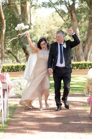 Joyful newlywed couple celebrating while walking down outdoor ceremony aisle surrounded by trees.