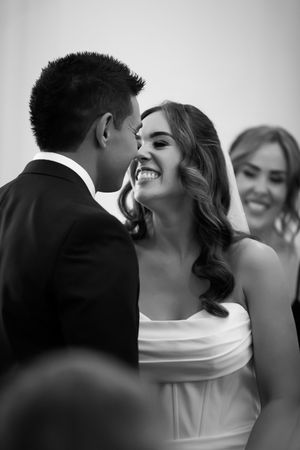 Black and white photo of a smiling bride and groom sharing an intimate moment during their wedding ceremony.