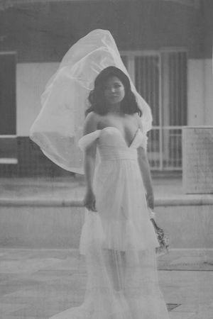 Black and white vintage photo of a bride in a flowing white gown with veil billowing in the wind outdoors.