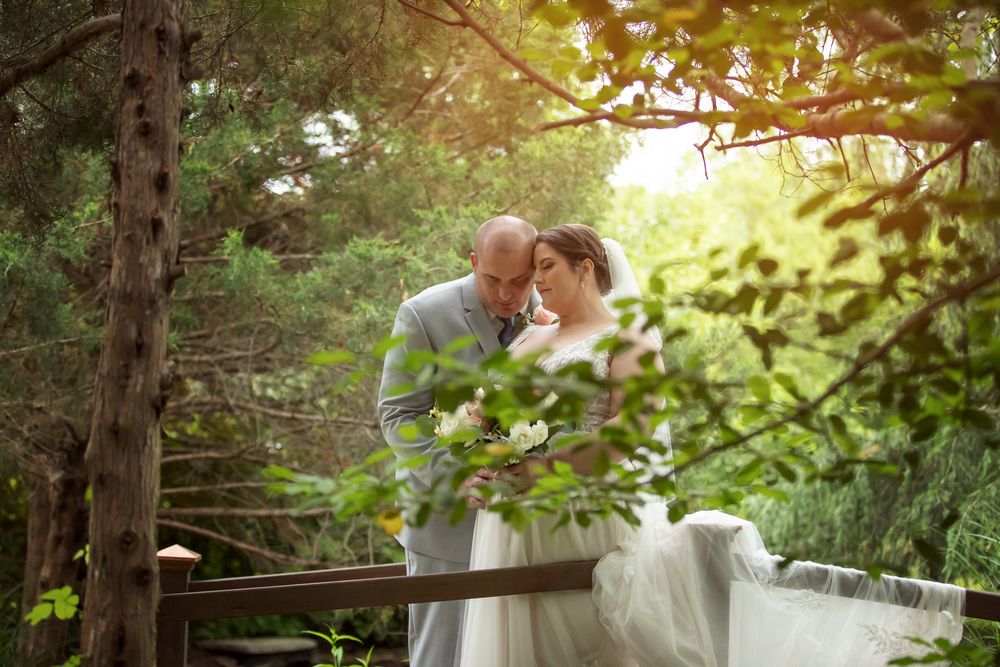 A tender moment between a bride and groom on a wooden bridge surrounded by lush green forest trees.