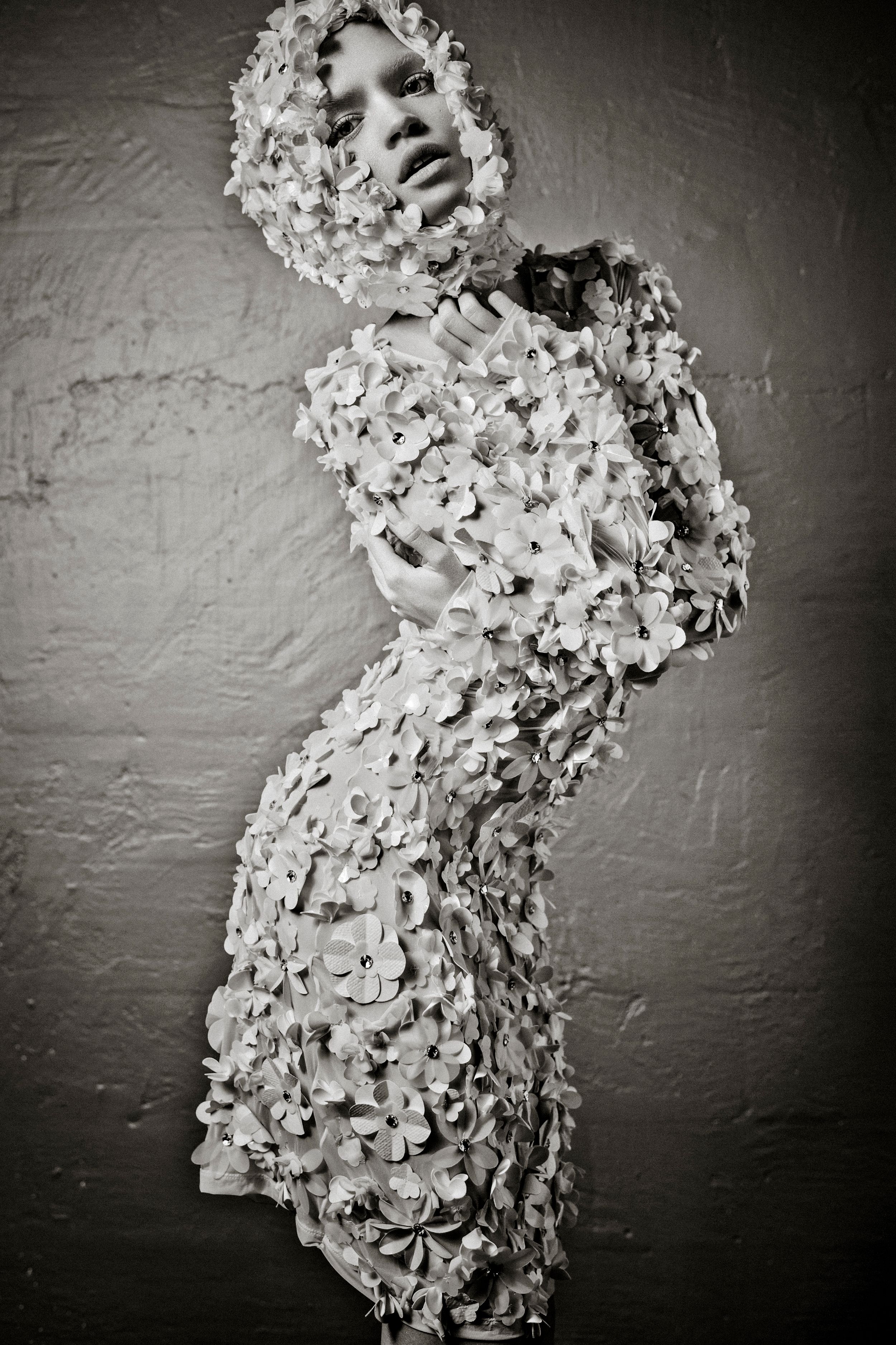 Black and white photo of a woman covered in delicate floral appliques from head to toe in an artistic fashion shoot.