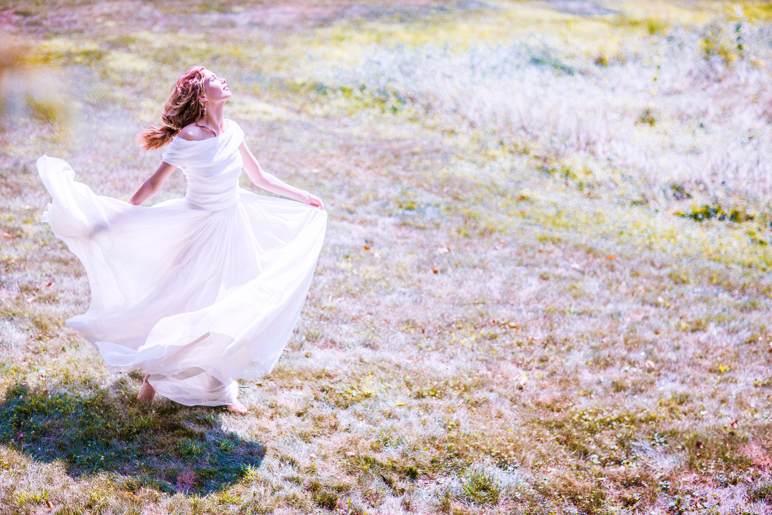 A young girl in a flowing white dress and floral crown twirls gracefully in a sunlit meadow.