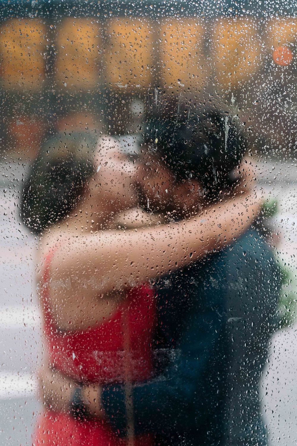 Couple kissing romantically through a rain-covered window, blurred silhouettes with water droplets on glass.