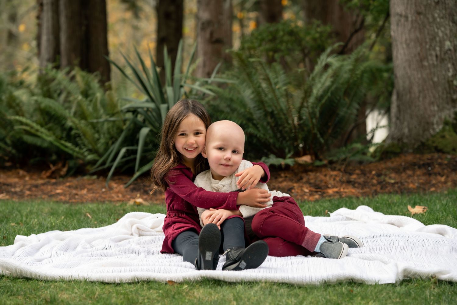 Family relaxing together on white blanket during outdoor photo session.