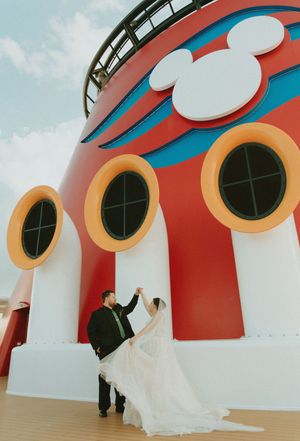 Bride and groom dancing on a Disney Cruise ship deck, with iconic Mickey Mouse logo and colorful portholes backdrop.