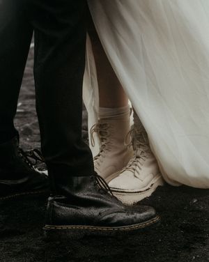 Close-up of wedding couple feet, groom in black Dr. Martens and bride in white lace-up boots beneath a white gown.