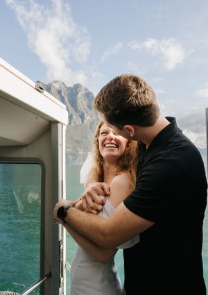 Happy couple embracing on a boat deck with stunning mountain lake views under a bright blue sky.