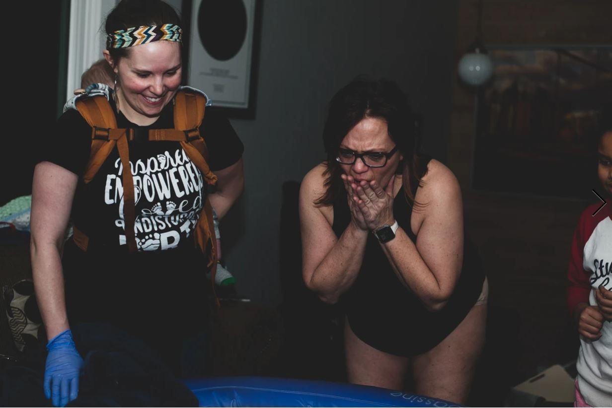 Support team watching anxiously during a water birth in dim lighting.