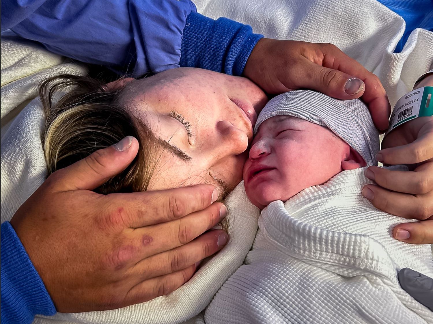 A newborn baby wrapped in white being cradled by gentle hands.