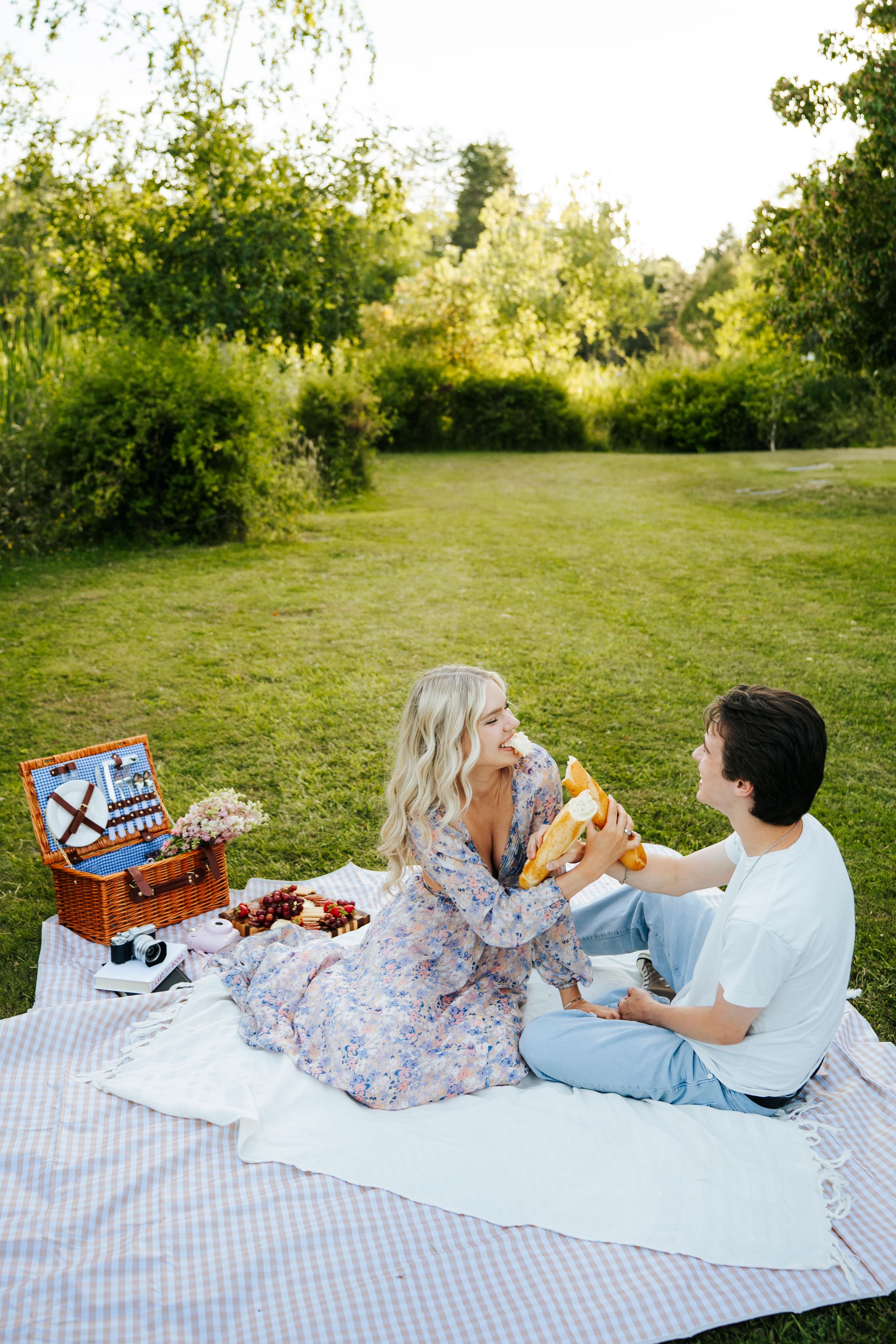 Couple enjoying a romantic picnic on a blanket in a lush green park, sharing food and smiling together.