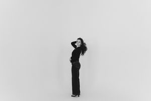Black and white full-length portrait of a woman in black outfit posing gracefully against a white background.