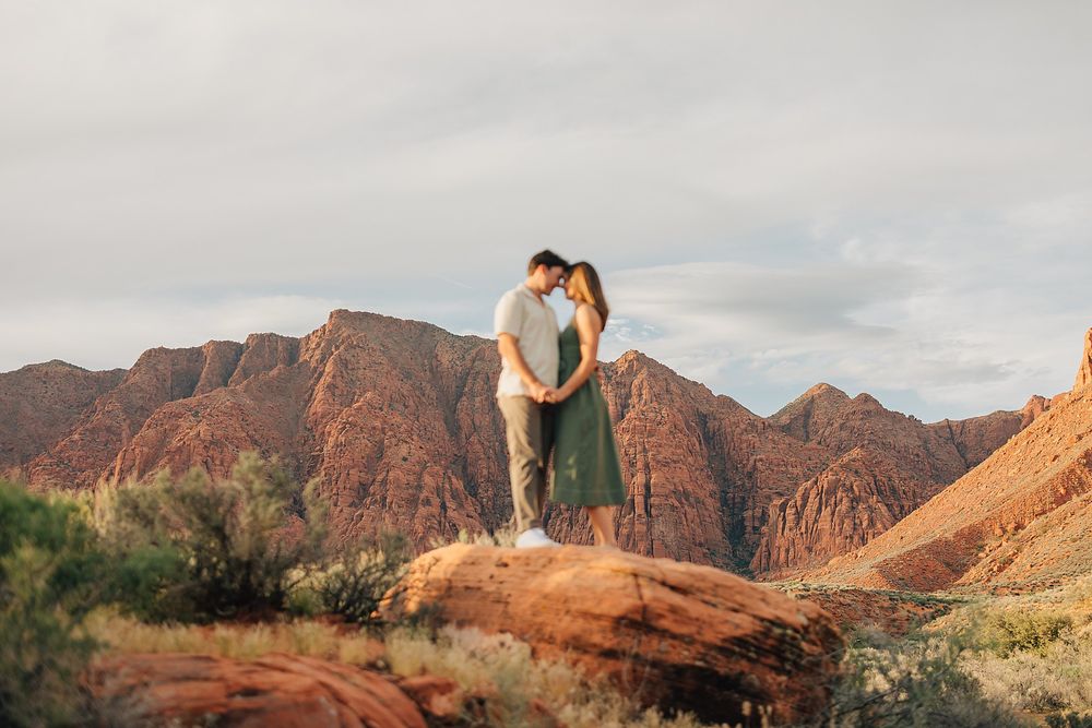 Couple embracing on red rock formation with stunning desert mountain backdrop at golden hour.