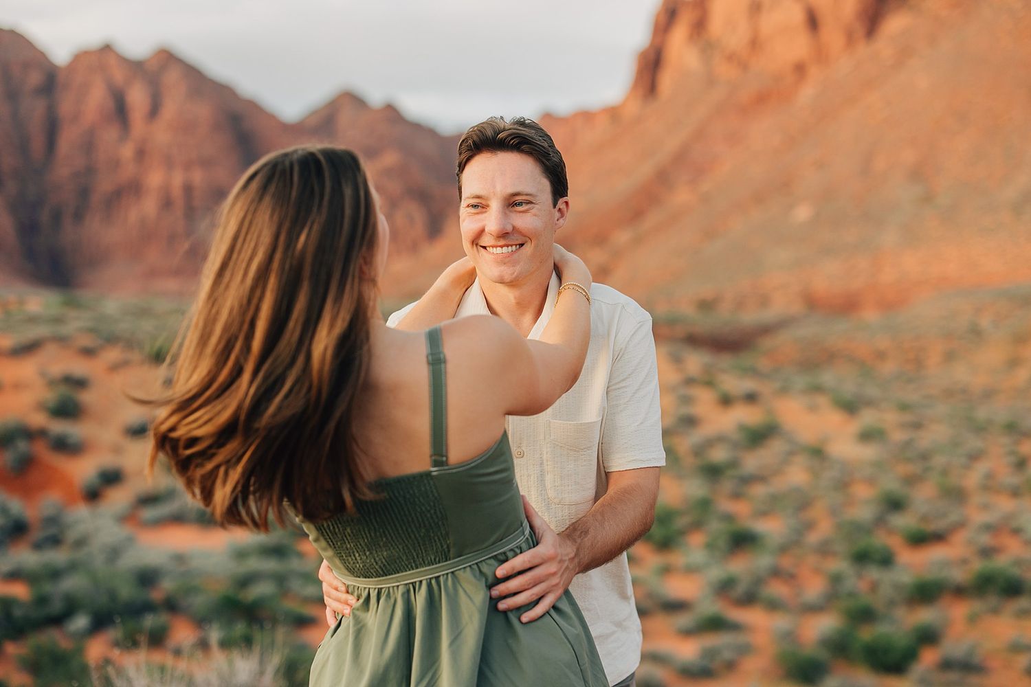 Two women embracing in a desert landscape with red rock mountains in the background during golden hour.