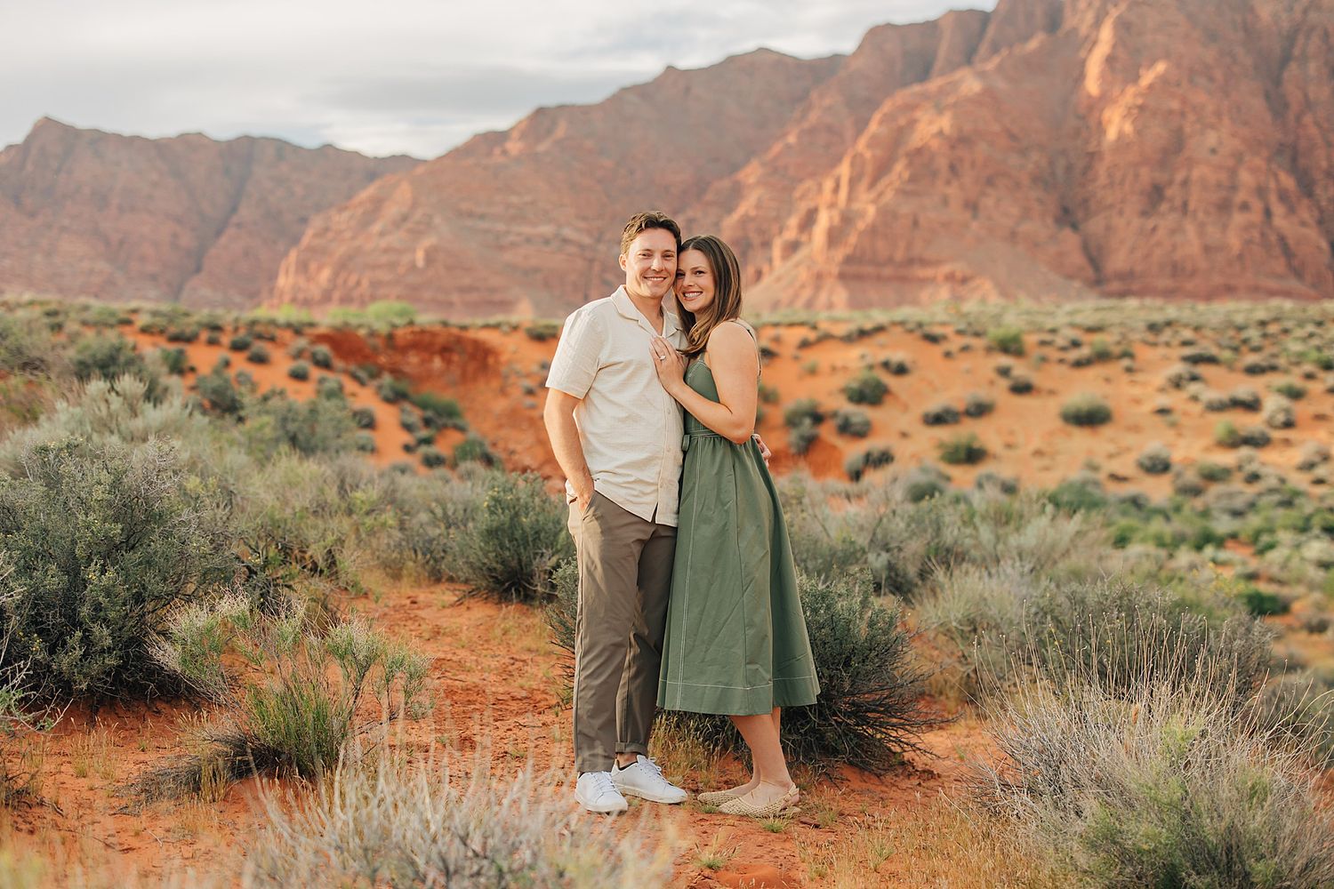 Couple embracing in desert landscape with red rock mountains and orange sand at sunset in Valley of Fire State Park.